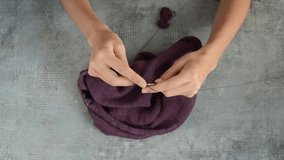 young womans hands knitting with gray metal needles and dark red cotton thread on stone table background, top view close-up full HD stock video footage in real-time