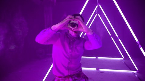 Professional Hip Hop break dancer . Stylish young man dancing with real strobe lights . Against colored background with triangle shape of led lights . Real decoration . Showing heart by fingers . 