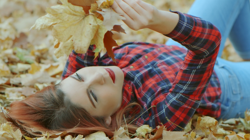 Portrait of beautiful woman with red hair lying in yellow autumn leaves. Female model enjoying life outdoors nature background 4k slow motion