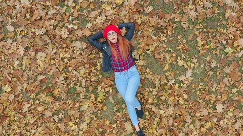 Aerial view of beautiful woman lying in yellow autumn leaves. Female model enjoying life outdoors nature background. Camera zooming out. 4k slow motion