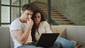 Portrait of young married couple watching scary video on notebook. Shocked man and woman expressing fear while looking laptop. Scared couple watching horror movie on laptop at home.