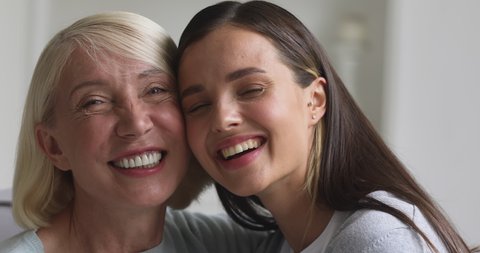 Happy affectionate two age generation women family laughing bonding together, smiling beautiful young daughter embrace old mature mother at home, parent and grown child love concept, closeup portrait