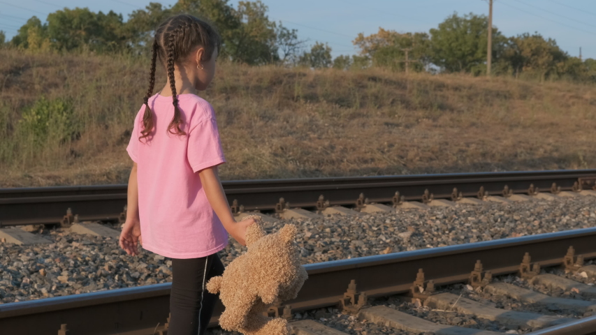 Child on railway. Little girl with a teddy bear walk along the railway.