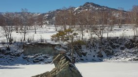 Aerial video view from backward moving drone on lonely Pine tree on rock on Altai river Katun in winter. Rocks called Dragon's teeth, Dragon crest, or Sartakpai Arrows.  Siberia, Russia