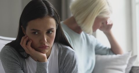 Upset stubborn young teen daughter thinking of apology and forgiveness, generation gaps and family conflicts after fight with older middle aged mom sitting turned back to parent avoiding talk concept