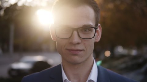 Lifestyle portrait of young attractive caucasian sales man, businessman smiling happy into the camera. Young businessman looking confident and successful, standing on the street, blurred sunlight on