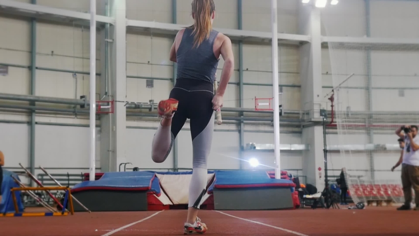 Pole vaulting indoors - a young woman with ponytail running up and jumping over the bar