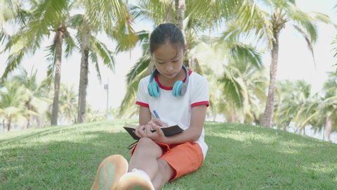 Young girl reading and writing a book while sitting in the park.
