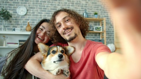Joyful girl and guy taking selfie with corgi dog having fun making funny faces showing hand gestures thumbs-up and v-sign. Youth and technology concept.