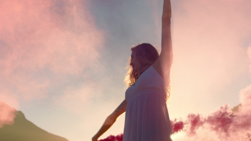 beautiful woman waving pink smoke grenade dancing on beach at sunrise celebrating creative freedom with playful dance movement