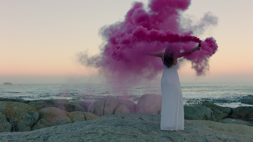 Woman holding pink smoke bomb dancing on beach in early morning celebrating creative freedom | Shutterstock HD Video #1041156211