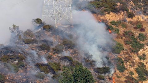 Thomas Fire. Southern California wildfire aerial view. Thick smoke over the burning forests. Open fire is seen among the trees. Power transmission tower on the hill is covered with smoke. 4K