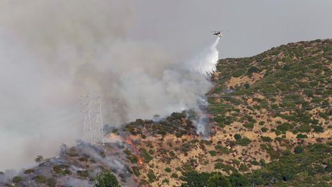 Getty wildfire. Brentwood, Los Angeles, California. A fire helicopter flying over a hill dumps water on a steaming forest. Firefighter aviation fight massive natural disaster in USA. 4K