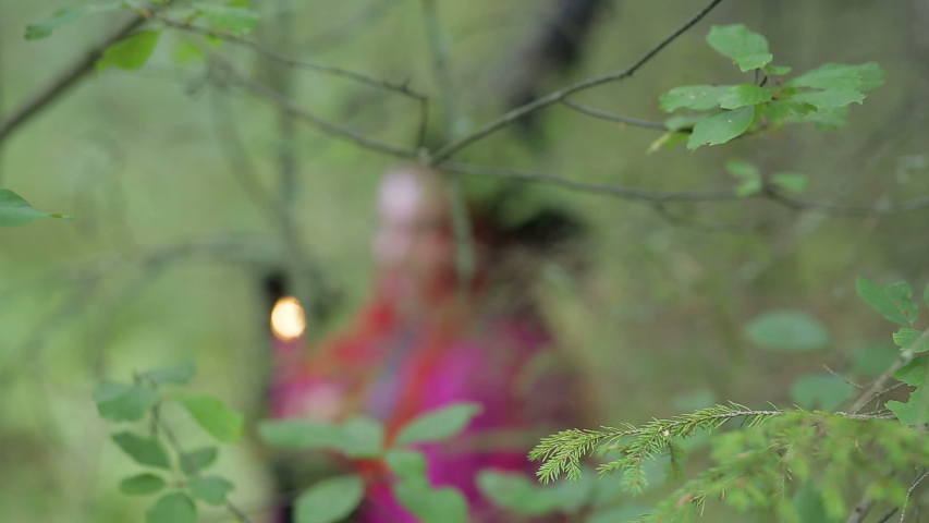 young witch with red hair and a black hat and cloak conjures with candles in the forest