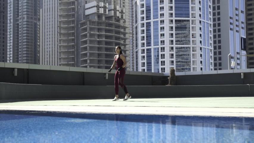 Beautiful young leggy kickboxer girl is training on the roof of the building along the pool doing high kicks and punches. City view of skyscrapers. Slow motion.