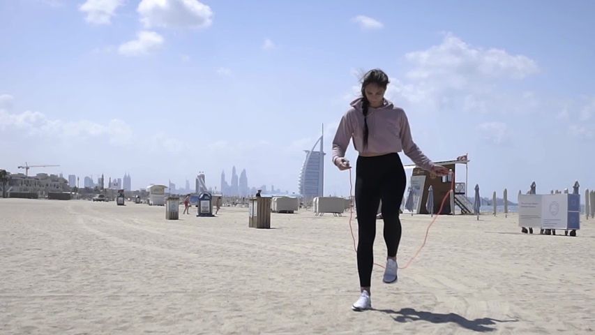 beautiful young leggy fit woman jumping rope on a sandy beach near the sea. Wide shot. Slow motion