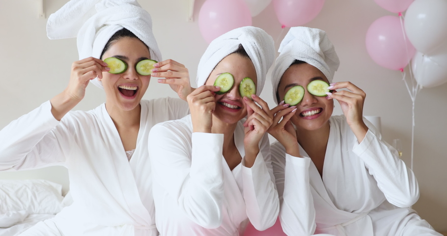 Funny happy young asian women friends wear white dressing gowns towels on head make cucumber facial skin care mask on eyes laugh having together look at camera on spa beauty salon party with balloons Royalty-Free Stock Footage #1041161701