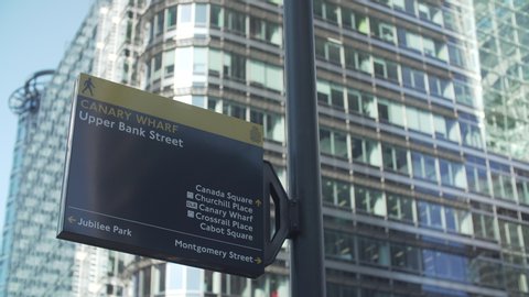 Close view with slow motion travelling of a Canary Wharf sign with buildings behind on a sunny day.