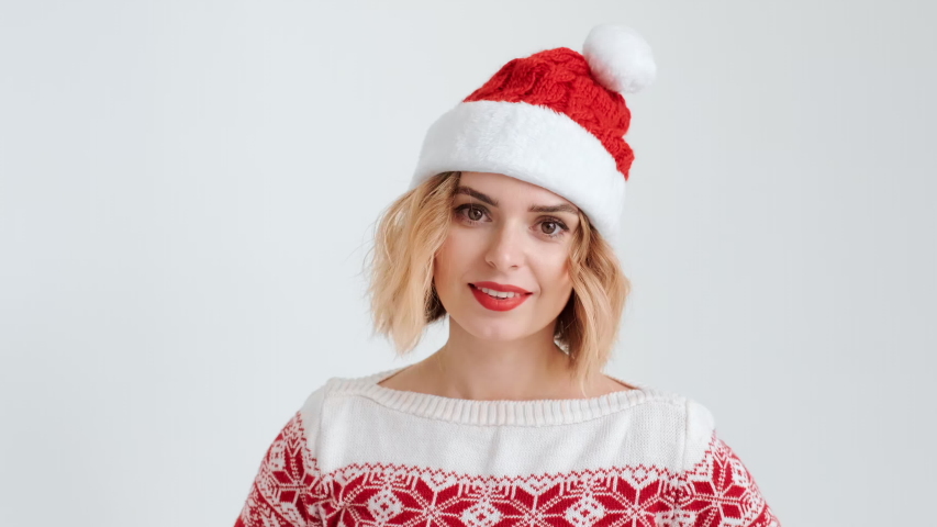 Christmas red cap costume young blond woman in smiling, dancing to music, looking at the camera in festive mood on white background. Santa's helper. Noel. Copy space. Christmas holidays. Emotions 