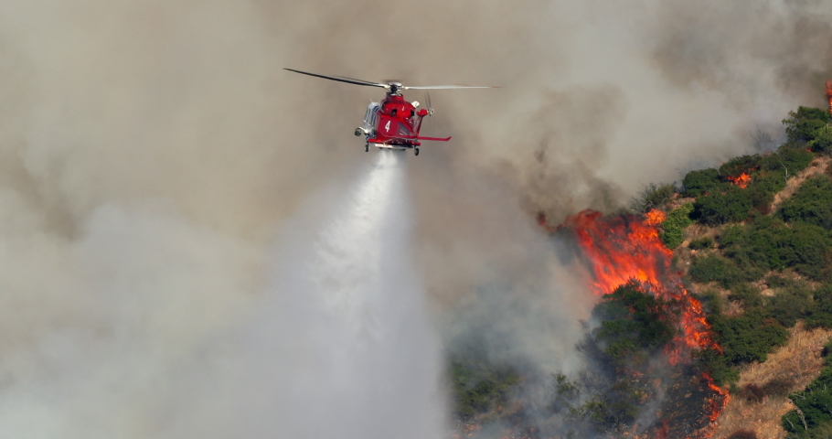 November 9, 2019. A firefighter helicopter approaches a burning area through a smoky sky and dumps tons of water onto a blazing forest. Hollywood hills. Warner Brothers wildfire. Los Angeles County.4K