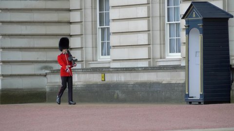 London, UK - April, 2019: London Buckingham Palace, Armed English Guard Marching and Guarding. Guards at Buckingham Palace. British guard in traditional red-black uniform. British guard patrolling.