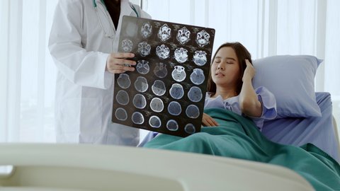 Asian woman lying in patient's bed Wearing blue patient gown See brain X-ray film In which expert doctor talk about the treatment in the hospital room that meet international standards. Health concept