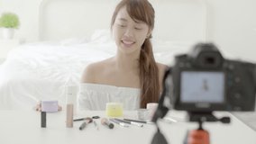 Beautiful young asian woman showing cream or lotion the cosmetic makeup with video and vlog at home, beauty girl blogger live review treatment with health on social media online.