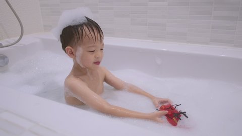 Cute little Asian 3 years old toddler baby boy child having fun sitting in bathtub playing with toy boat in the bathroom at home, Happy kid enjoying bath time, Kid be left alone in the bath