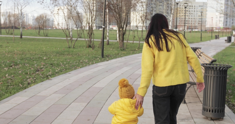 Mom with a baby in a yellow jacket teaches to ride a scooter in a city park