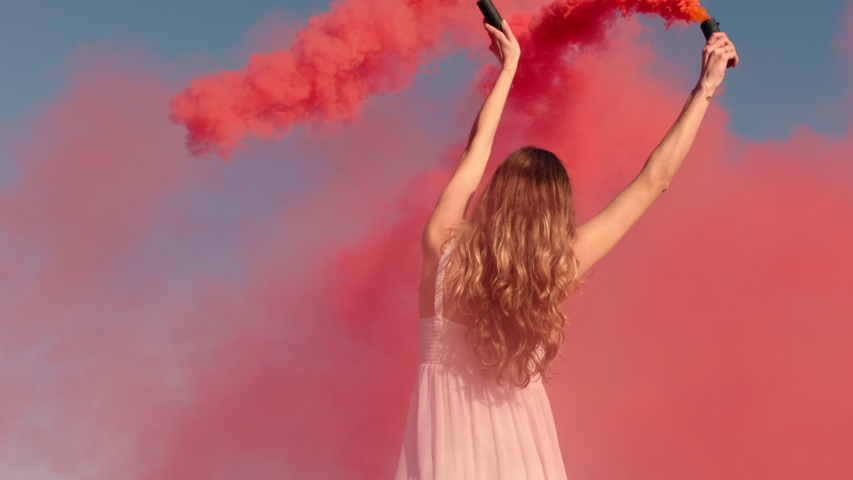 woman waving pink smoke bomb on beach at sunrise slow motion