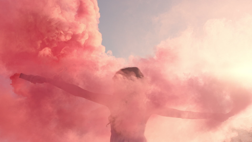 Woman dancing with pink smoke bomb on beach at sunrise celebrating creative freedom with playful dance spin slow motion