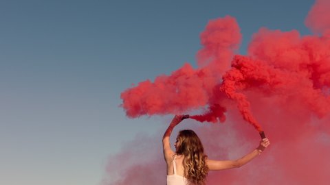 woman dancing with pink smoke bomb on beach at sunrise celebrating creative freedom with playful dance spin slow motion