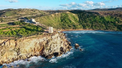 Aerial view of Ghajn Tuffieha Tower and beach. Sunset, blue sky, greeny hill, waves in the sea. Winter. Camera move forward. Malta