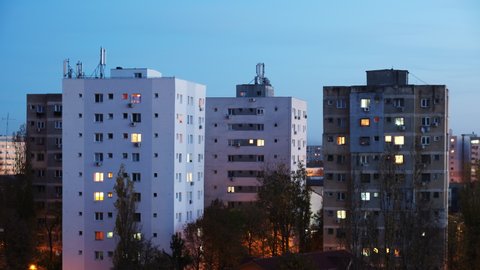 Time lapse of windows light on a multi-storey apartment building from blue hour to night. Buildings with renovated exteriors near old communist era buildings, at night.