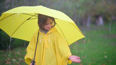 Cute little girl with a yellow umbrella in the rain. A child in a raincoat is having fun in the rain. Rainy weather.	