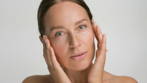 Close-up beauty portrait of young woman with smooth healthy skin, she gently touches her face with her fingers on white background