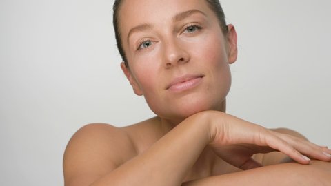 Close-up beauty portrait of young woman with smooth healthy skin, she opens her eyes and raises her head on white background