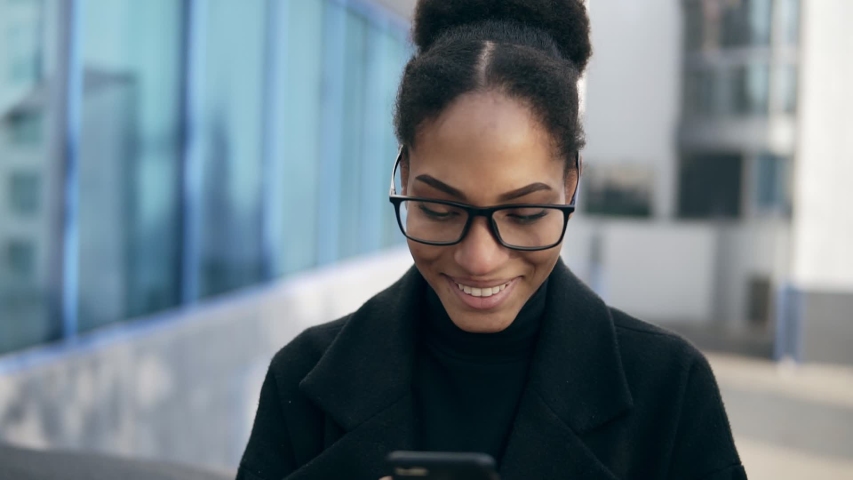 Shocked African American woman gots message from ex, gasps from surprise and excitement, reads stunning news on mobile phone. Excited girl standing outdoors, on the street. Wearing black clothes and Royalty-Free Stock Footage #1041220483