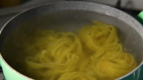Wheat pasta of format tagliatelle a boiling water in mint green pot, close up. Cooking italian pasta
