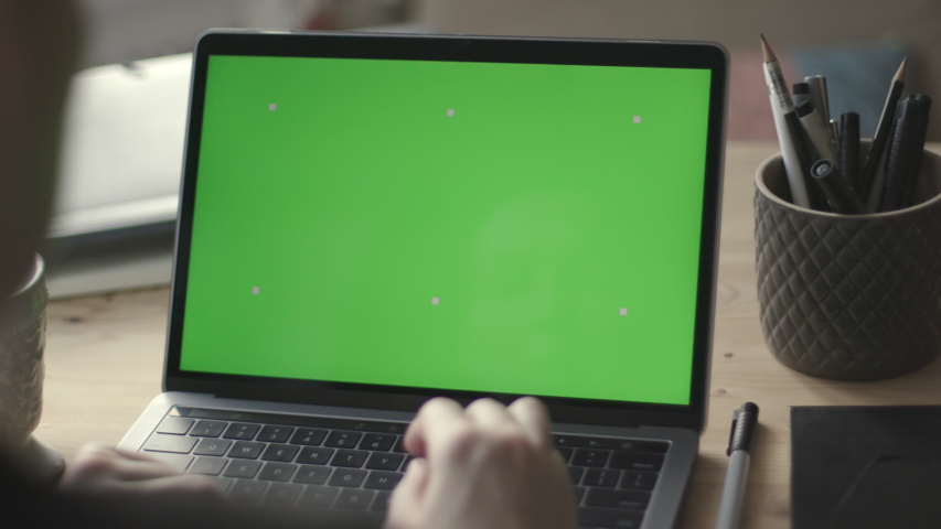 Over the shoulder shot of young woman working on modern laptop with green screen mock-up. Hands on keyboard. | Shutterstock HD Video #1041228292