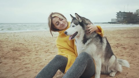 Young beautiful female walking with siberian husky dog on the beach. Woman runs and plays with husky dog 