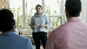 Confident team leader talking to employees. Serious young woman standing and communicating with team. Business meeting concept