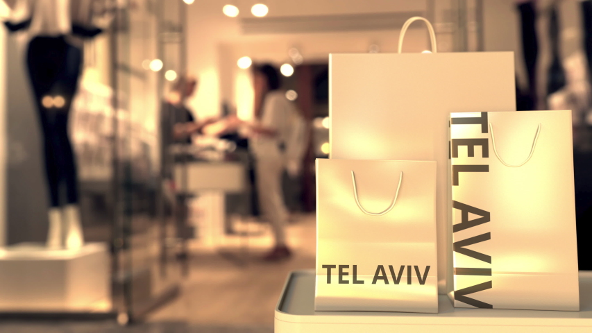 Paper shopping bags with TEL AVIV text against blurred store. Israeli shopping related clip