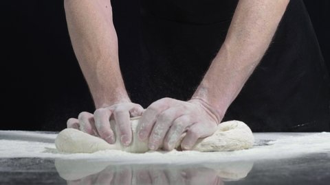 close up shot of man hands kneading bread dough at the metal table on a black background. Slow Motion 4k