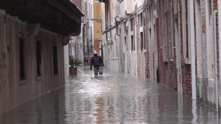 VENICE, ITALY - November 12, 2019: Man walking on the narrow streets during flood (acqua alta) in Venice, Italy. Venice high water. 4k