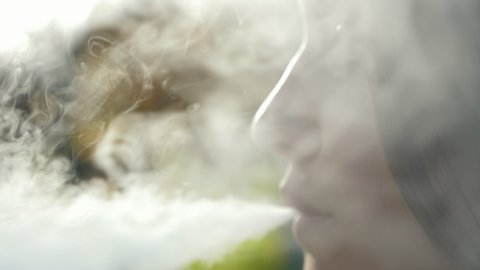 Closeup face of cute caucasian woman vaping e-cigarette outdoors