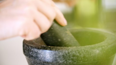 Home cook using a pestle and mortar to crush coriander seeds into a powder. Pouring the powder into a black bowl. 
