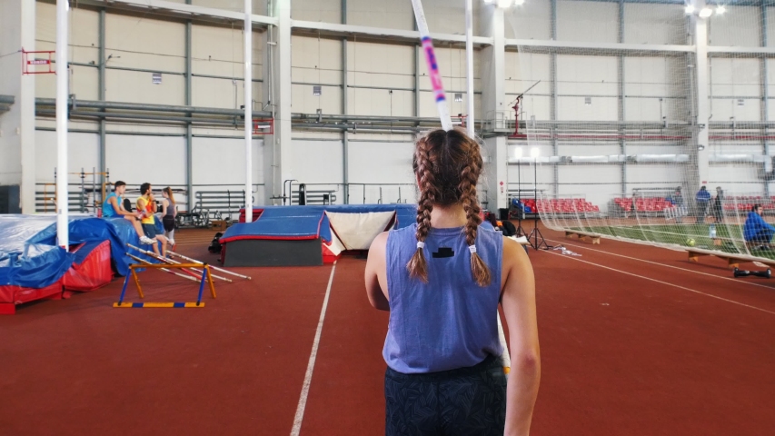 Pole vaulting in the indoors stadium - young woman with pigtails jumping over the bar
