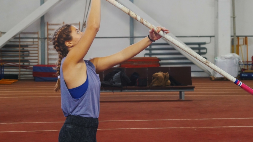 Pole vaulting indoors - young woman with pigtails preparing for the jump - running up - jumping over the bar
