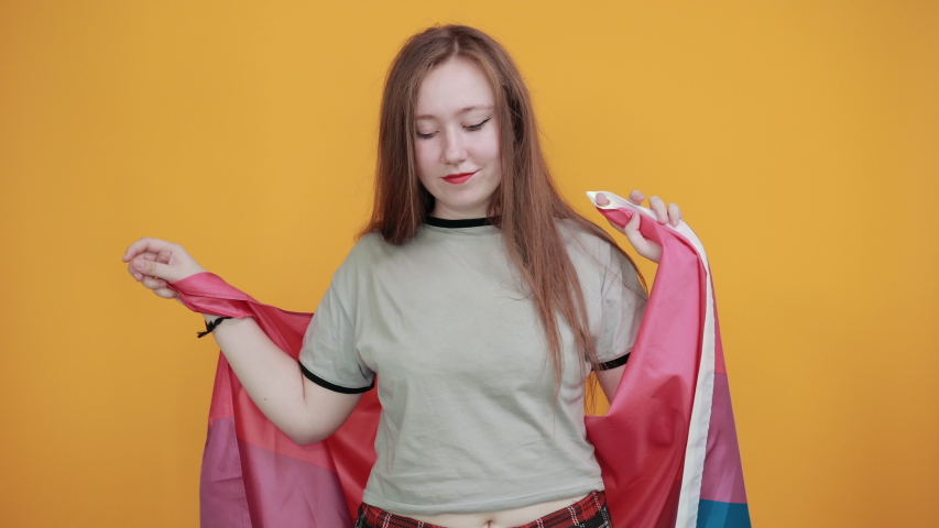 Portrait of excited young woman in gray casual shirt pointing index fingers aside, showing victory gesture, looking camera isolated on orange wall background in studio. People lifestyle concept.